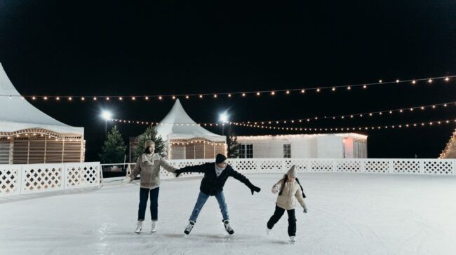 A family enjoying ice skating together on an outdoor rink at night under festive string lights. - Photo by cottonbro studio on Pexels