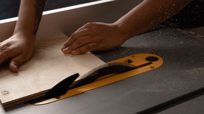 Close-up of person using a table saw to cut wood in a workshop setting. Sawdust in the air. - Photo by Mario Spencer on Pexels